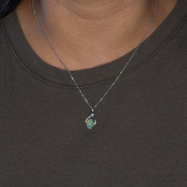 An Ethiopian opal cabochon flashes with a lively play of colour at the centre of this solid 14K white gold pendant, framed...