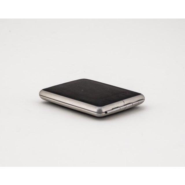A vintage cigarette case made of stainless steel with a black leather inlay on the outside. The object has been...