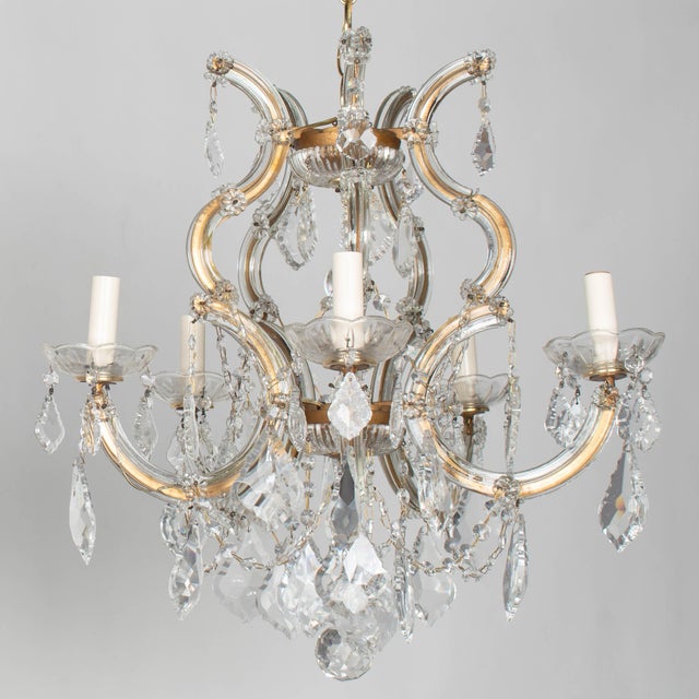 A set of two vintage Maria Theresa style five-light crystal chandeliers. Each with curving, ornate gilt metal frame clad...