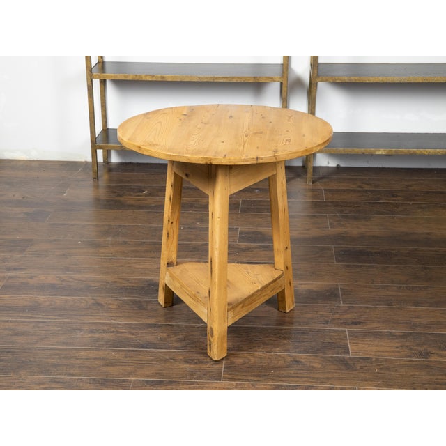 An English rustic pine cricket table from the 19th century, with circular top and triangular shelf. Created in England...