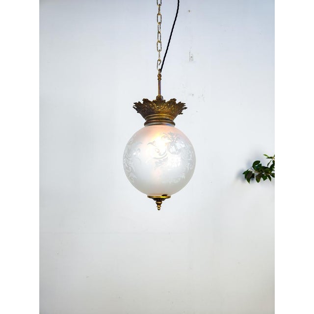 Dutch art nouveau globe pendant light with a decorative design etched into the glass. The globe is suspended from a period...