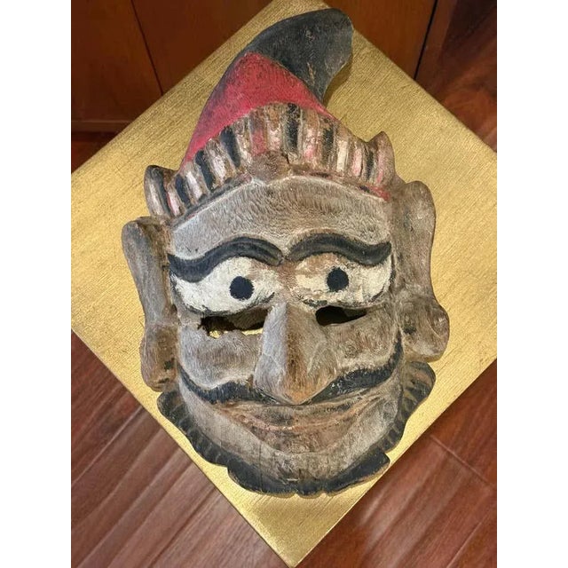 An expressive tribal mask with pronounced brows, stylized features, and traces of red and black pigment, reflecting its...