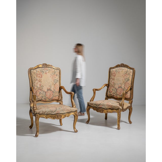 A decorative pair of Louis XV armchairs combining gilded wood frames with tapestry upholstery, reflecting the Rococo...