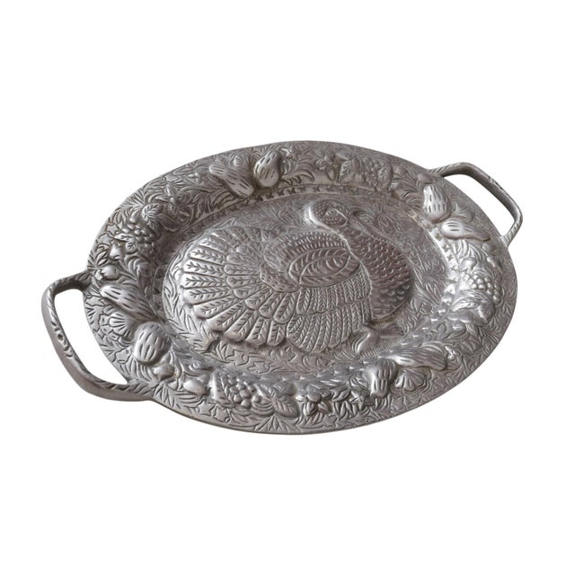 An oval serving platter in pewter, embossed with a turkey surrounded with foliage, fruit and berries, in high relief. The...