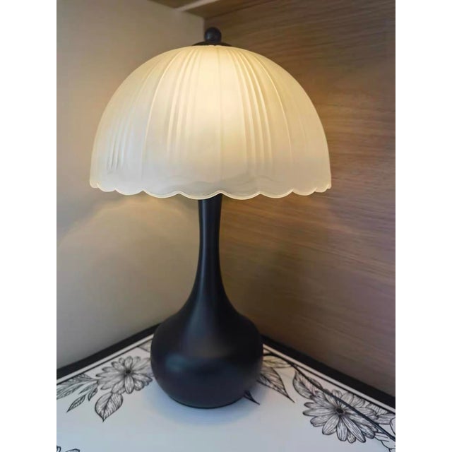 The shade features milk-white pleated petal texture (soft curved edge), the lamp body is a matte black teardrop shape with...