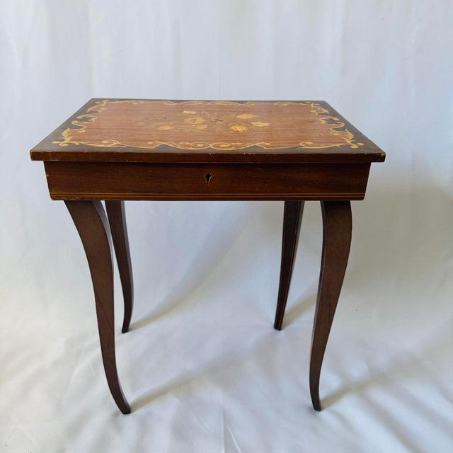 Vintage Italian inlaid wood music box accent table. Made of wood with inlaid floral marquetry design. The music box is...