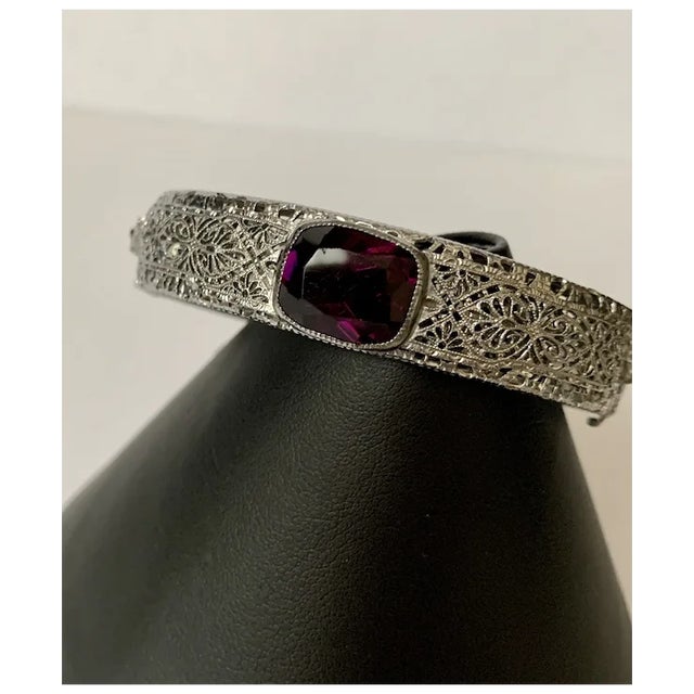 Amazing Art Deco filagree and purple glass bangle. There are two small rhinestones on either side of the faceted, bezel...