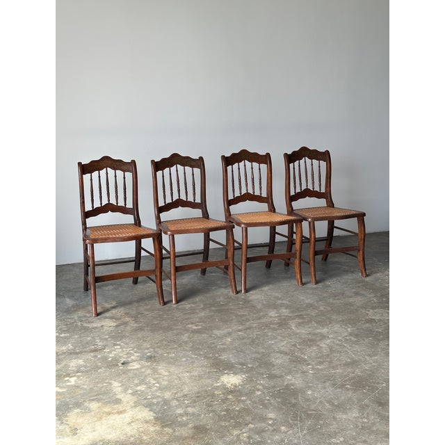 A set of four dining chairs with turned spindle backs, shaped crest rails, and cane seats set on gently splayed saber...