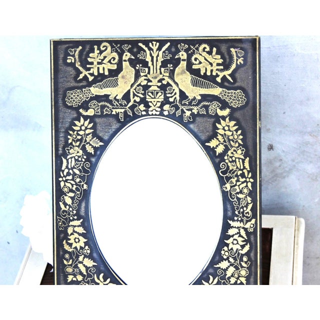 Decorative vintage table mirror featuring an elaborate black metal frame with contrasting gold-tone engraved decoration....