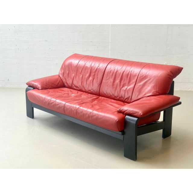 A striking vintage sofa by ligne roset featuring a bold combination of red smooth leather and a solid, black-painted...