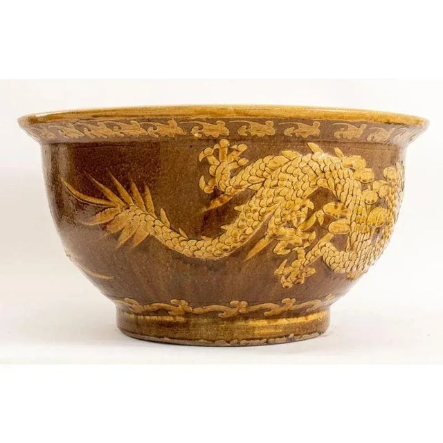 A Chinese glazed ceramic ochre jardiniere with a low relief circling the planter of two five-toed dragons. The pot is wide...