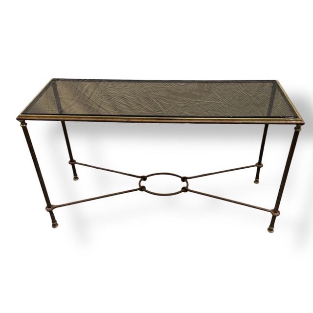 An elegant console table featuring a glass top and a two-tone steel and brass frame with X-stretcher base. Maison Jansen...