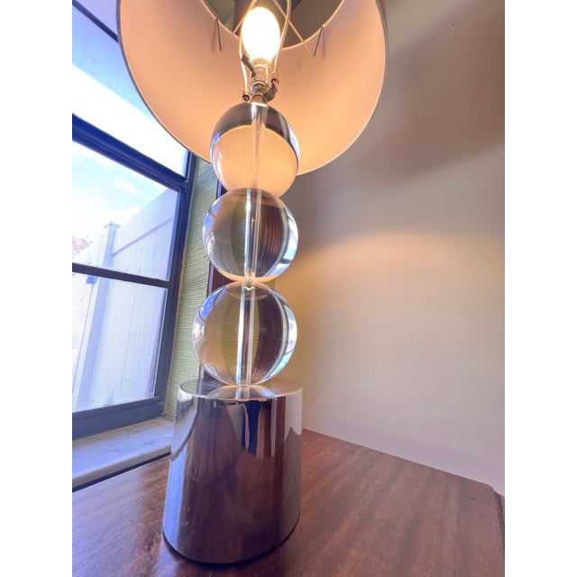 Sleek modern table lamp featuring three stacked clear orb spheres on a central rod, anchored by a polished chrome...