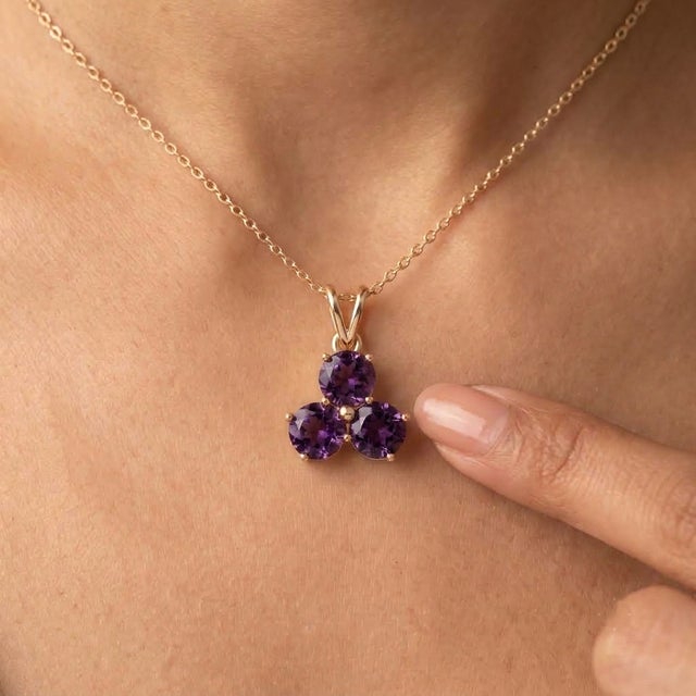 A regal three-stone design featuring round-cut natural amethysts arranged in a graceful trefoil formation, secured in a...