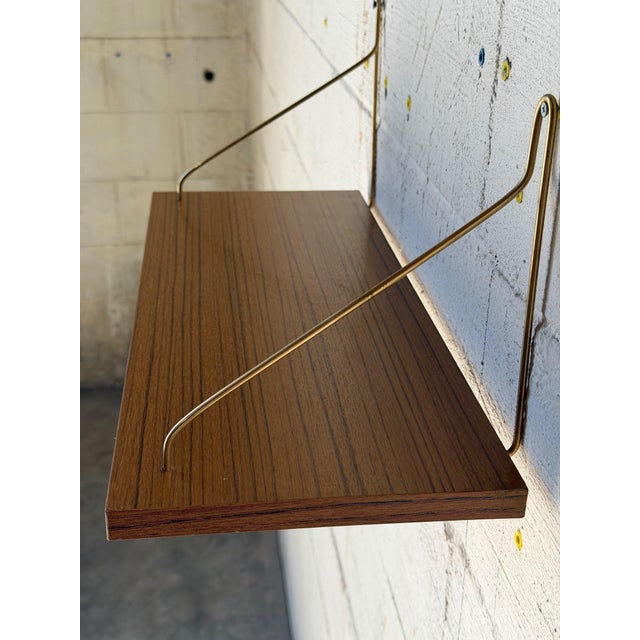 Vintage Mid-Century Modern floating teak wall shelf featuring a warm wood finish and elegant brass-toned metal brackets....