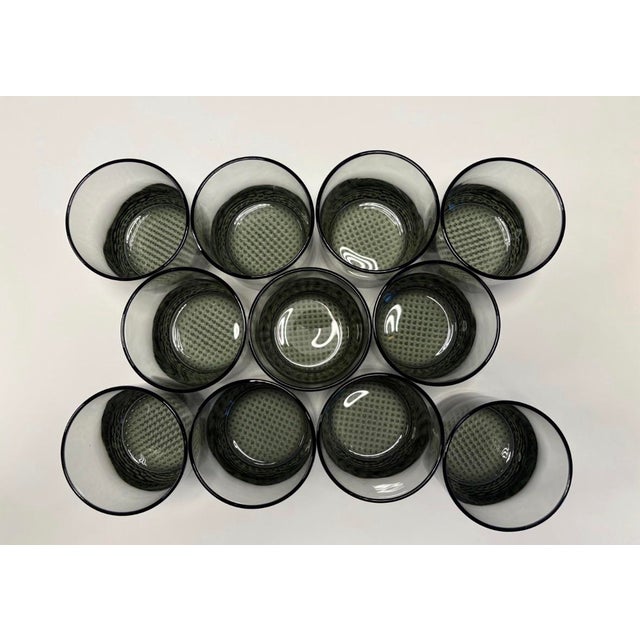 A striking set of twelve mid-century Scandinavian–style smoked glass rocks tumblers, distinguished by their weighted bases...
