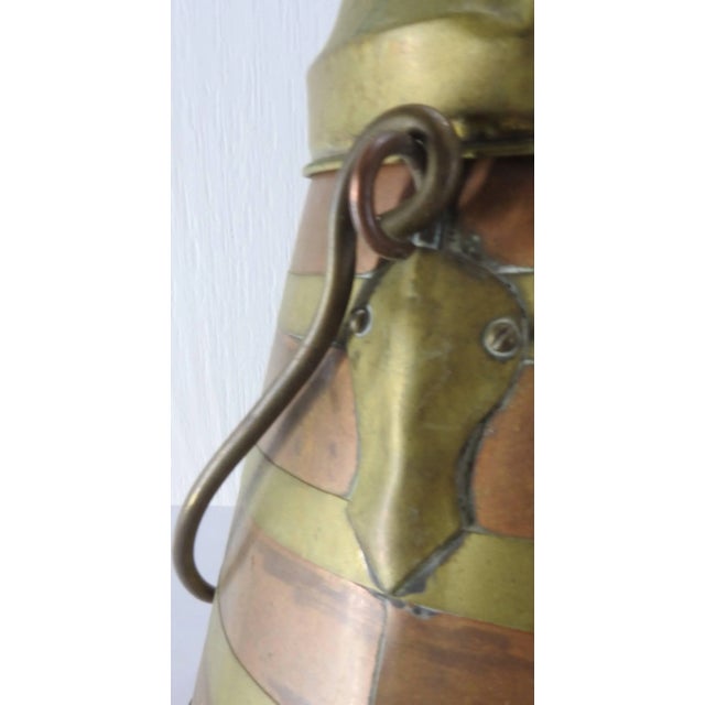 Bands of copper and brass form this Arts & Crafts tapered vessel. It sits on three feet and has a brass lid and handle. It...