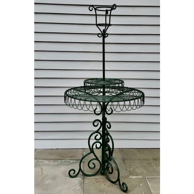 A tall vintage wire and wrought iron plant stand with scrolling ironwork, tiered circular shelves, and a garden-ready...
