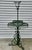 A tall vintage wire and wrought iron plant stand with scrolling ironwork, tiered circular shelves, and a garden-ready...