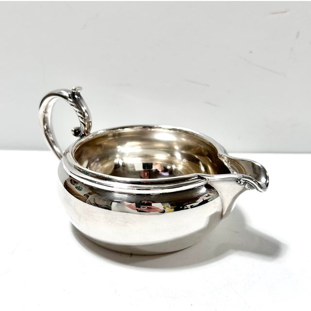 A classic vintage Reed & Barton silverplate sauce boat featuring a rounded body, defined spout, and elegant scroll handle....