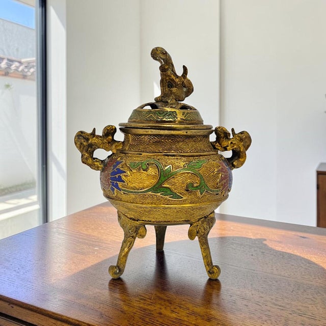 A mid-20th-century Japanese tripod incense burner, or kōro, cast in copper alloy and decorated with polychrome champlevé...