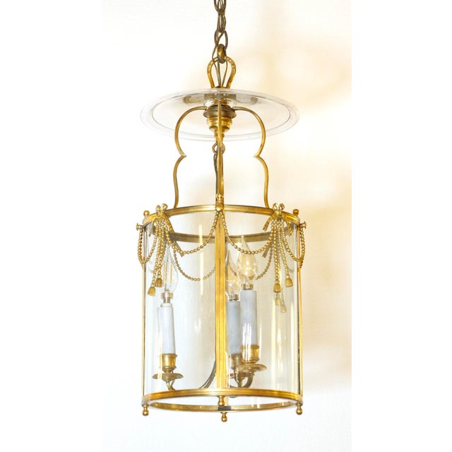 Antique gilded bronze French cylinder lantern pendant light with ribbon and tassel detailing and a clear glass top. This...