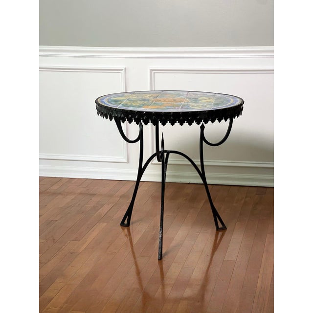 Italian Mediterranean hand-painted ceramic tile top table with a sculptural black iron base, circa 1950s. The top bursts...