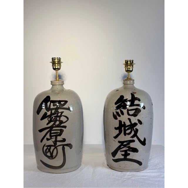 Pair of lamps crafted from gray-white glazed stoneware sake jars (tobin), Japan, first half of the 20th century. Each jar...