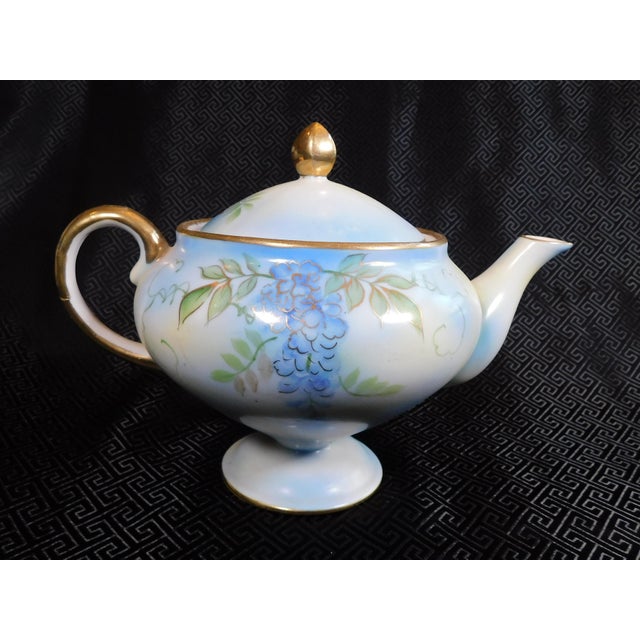 This is a footed blue teapot from Shofu Japan. It has a design of purple flowers on a blue background with green leaves...
