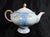 This is a footed blue teapot from Shofu Japan. It has a design of purple flowers on a blue background with green leaves...