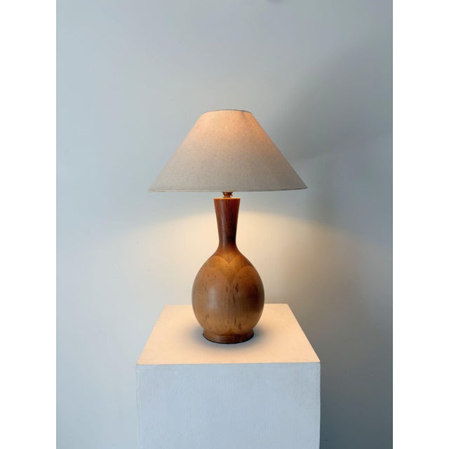 A sleek turned wood table lamp from the Mid Century. The curvature of the base is echoed and emphasised by skilled inlay...