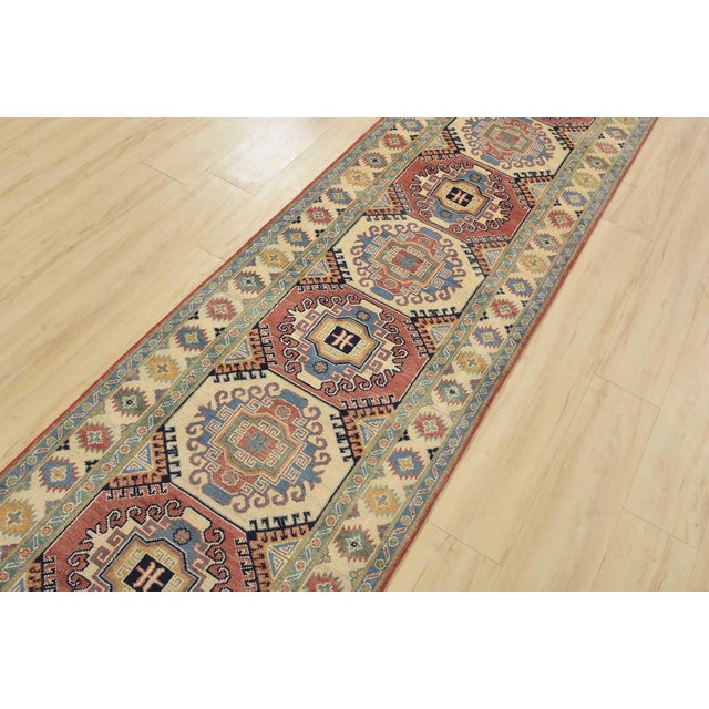 A tribal Caucasian Kazak runner hand-knotted with fine wool on a cotton foundation. This rug features a row of geometric...