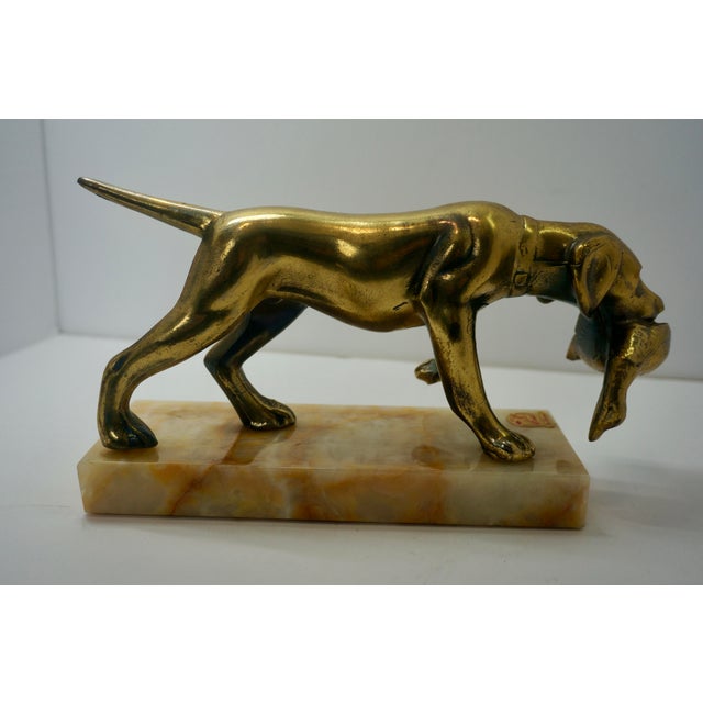 A striking mid-century brass sculpture depicting a pointer or retriever hunting dog proudly clutching a game bird in its...