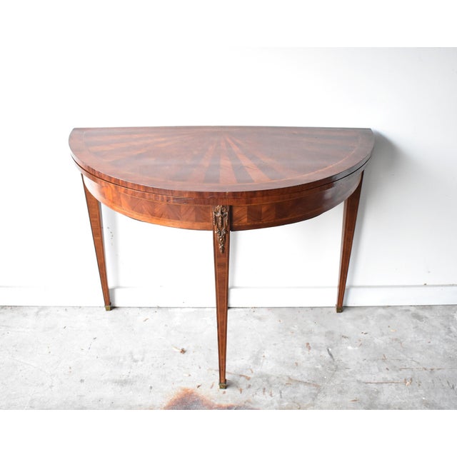 An antique French demilune card table in the neoclassical Sheraton style, with an inlaid marquetry sunburst top and...