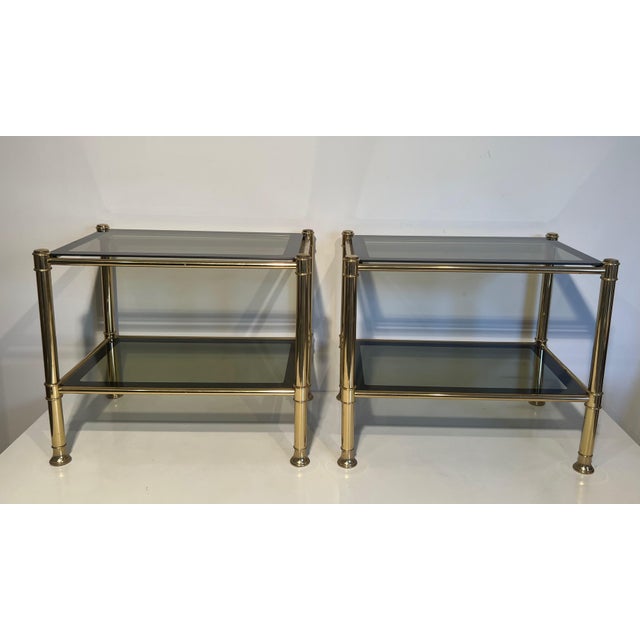 This pair of side tables is made of brass with smoked glass shelves. It is a French work. Circa 1970