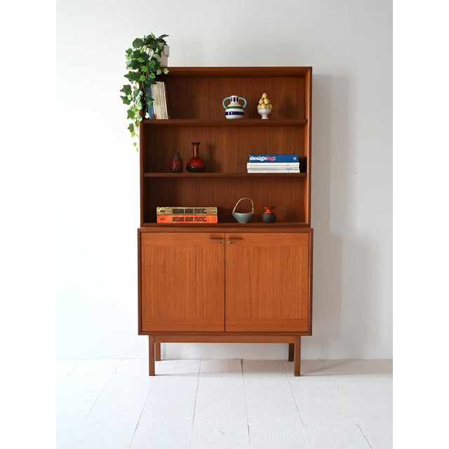 Teak bookcase composed of closed compartments and open shelving. Inside the space is divided by shelves. The lower part...
