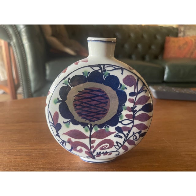The Royal Copenhagen vase depicts a stylized blue flower surrounded by blue and purple leaves. It is round in shape...