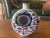 The Royal Copenhagen vase depicts a stylized blue flower surrounded by blue and purple leaves. It is round in shape...
