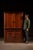 A substantial two-piece primitive corner cabinet constructed in solid wood with a warm reddish-brown finish and simple...