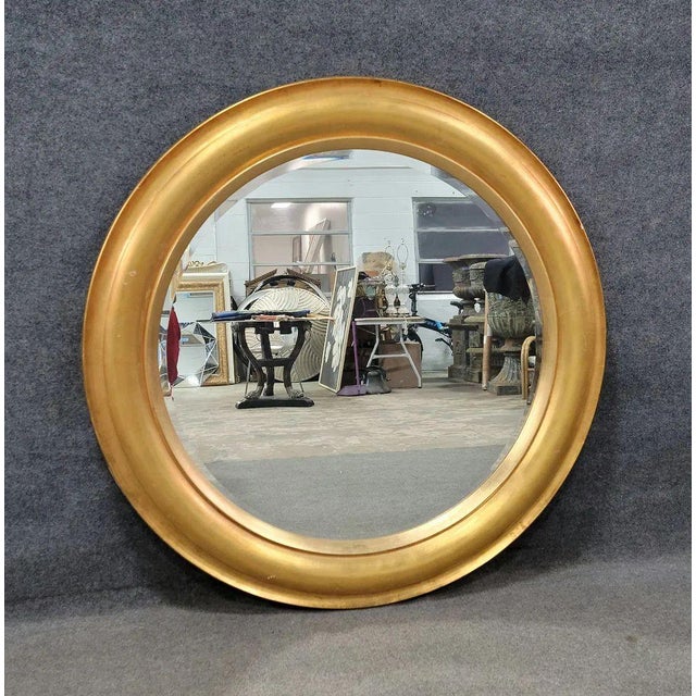 A striking oversized round mirror featuring a deeply molded gold leaf frame with a warm, softly aged finish. The...
