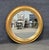 A striking oversized round mirror featuring a deeply molded gold leaf frame with a warm, softly aged finish. The...