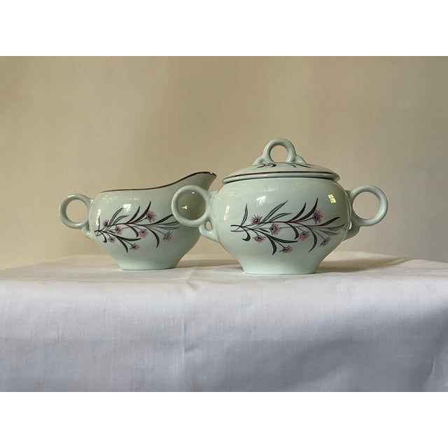 A vintage creamer and covered sugar bowl set in pastel green stylized pink & grey flowers and a silver trim. Creamer...