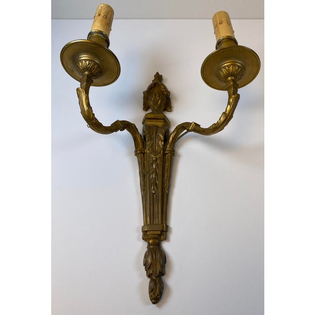 A beautiful and highly decorative pair of French Louis XVI style bronze two-light wall sconces, exhibiting the refined...