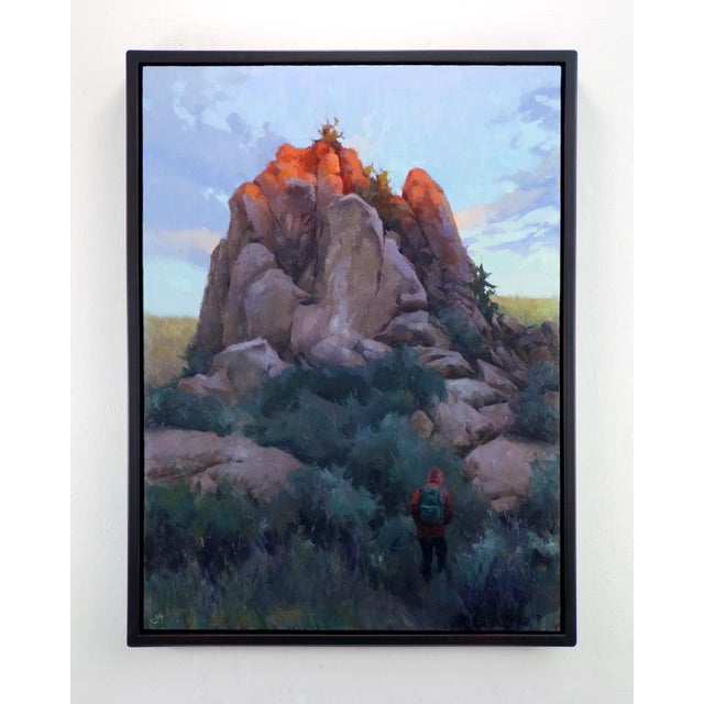 This oil painting depicts a solitary figure standing before a majestic rock formation, bathed in warm, golden light as the...