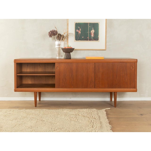 Classic sideboard from the 1960s. High-quality teak veneer body with two sliding doors, four drawers, two shelves, and...
