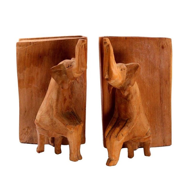Hand-carved from solid sycamore, each bookend in this pair depicts a stylised elephant seated upright beside a thick...