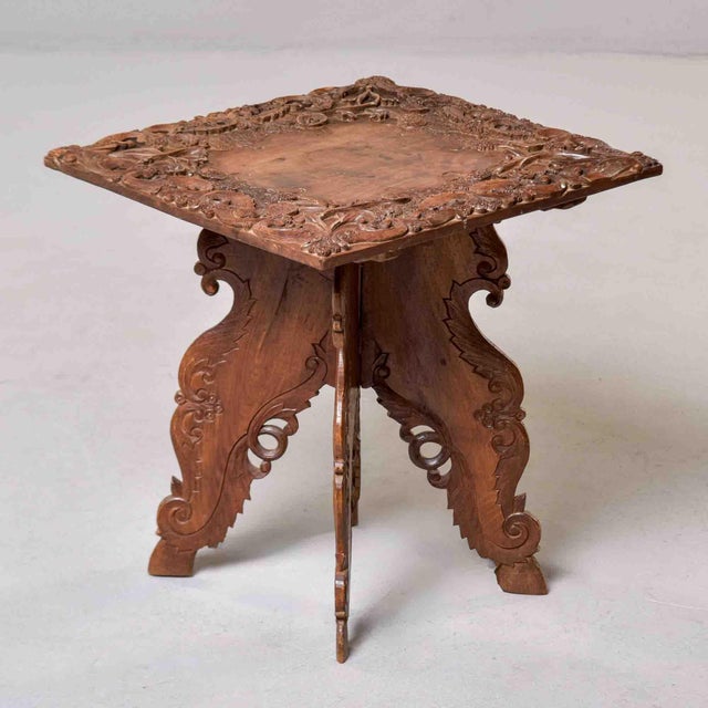 A richly carved Anglo-Indian occasional table featuring a square top with deeply carved foliate and floral border...