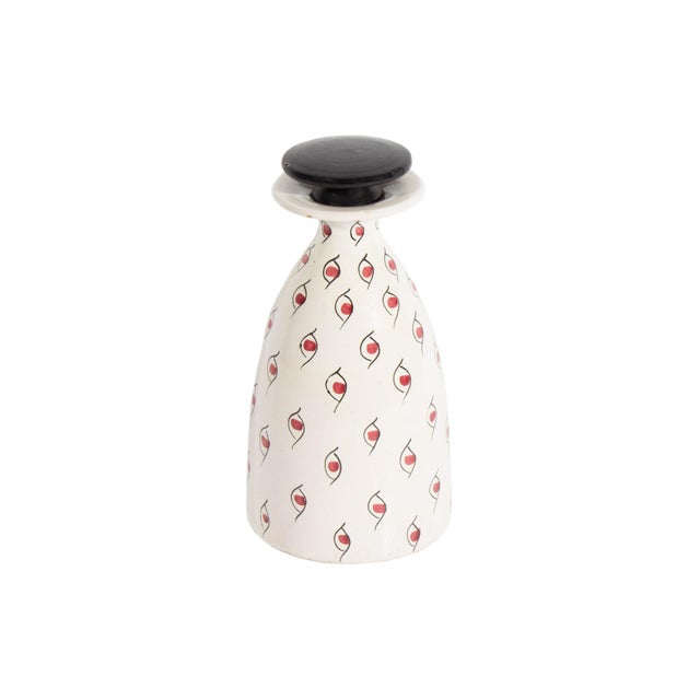 A ceramic decanter produced by Bitossi. Made in Italy, the decanter has a flat round stopper, a white body, and red and...