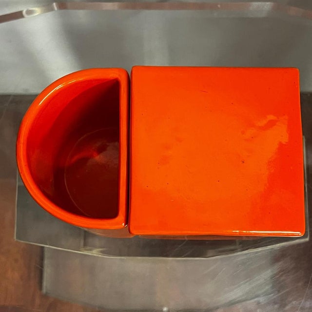 Large orange ceramic storage box, consisting of two containers, one with lid, the other crescent-shaped, open. Produced by...