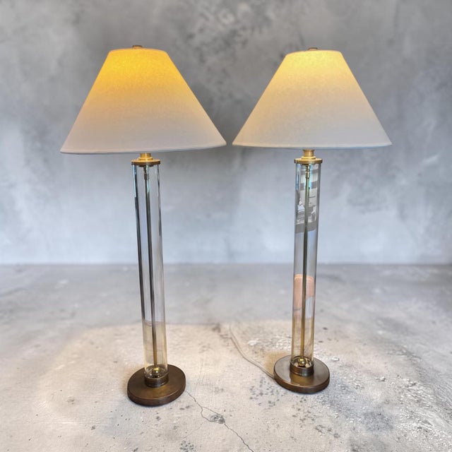 An elegant pair of signed Ralph Lauren Home table lamps featuring substantial tubular glass columns anchored by solid...